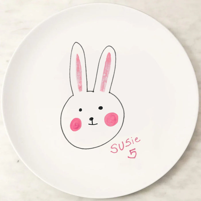 White kids melamine plate with a hand-drawn rabbit face and the name 'Susie' on a light wooden surface.