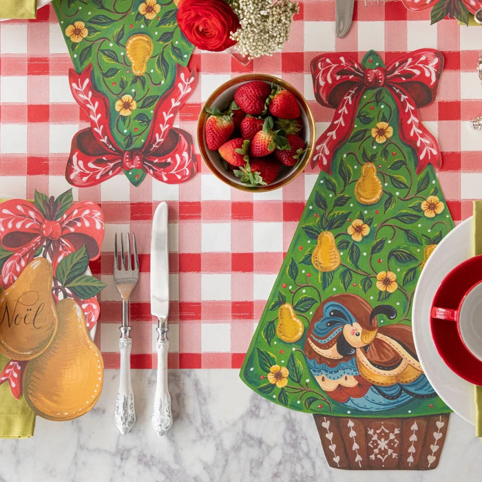 Decorative Christmas table setting with tree-shaped placemats, strawberries, and cutlery on a checkered tablecloth.