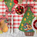 Decorative Christmas table setting with tree-shaped placemats, strawberries, and cutlery on a checkered tablecloth.