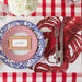 Place setting with lobster-themed placemat, checkered plates, and cutlery on a red and white checkered tablecloth.