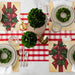 Christmas-themed table setting with red and green decorations on a checkered tablecloth.