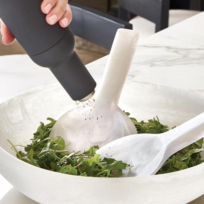 Person using a pepper grinder over a bowl of greens on a marble surface