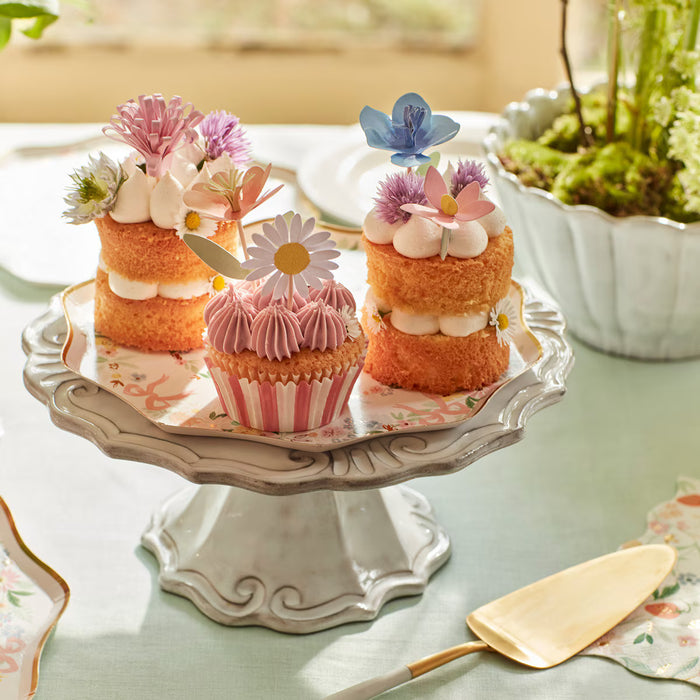 Decorative cake stand with small cakes and cupcakes on a light green surface.