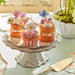 Decorative cake stand with small cakes and cupcakes on a light green surface.