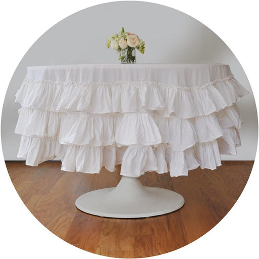A white ruffle round tablecloth on a table with a floral centerpiece.
