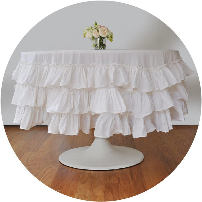 A white ruffle round tablecloth on a table with a floral centerpiece.