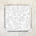 A set of white and silver Chantilly lace luncheon napkins displayed on an acrylic napkin holder.