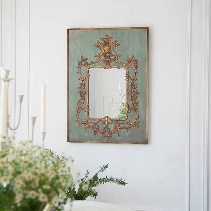 Decorative mirror with ornate frame on a white wall, with flowers and candles in the foreground.