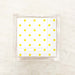 A clear napkin holder box containing yellow and white polka dot cocktail napkins displayed on a marble background.