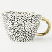 White mug with black dot pattern and gold handle on a white background