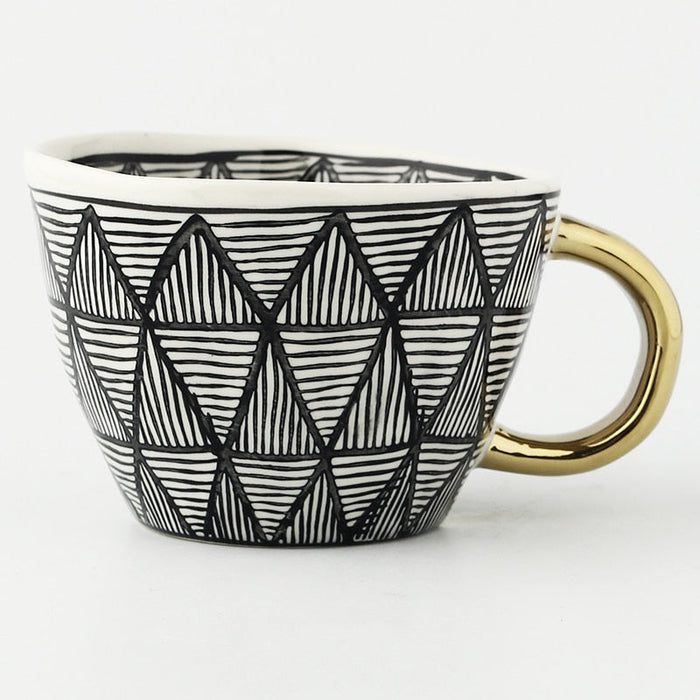 Ceramic mug with black geometric pattern and gold handle on a white background