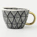 Ceramic mug with black geometric pattern and gold handle on a white background