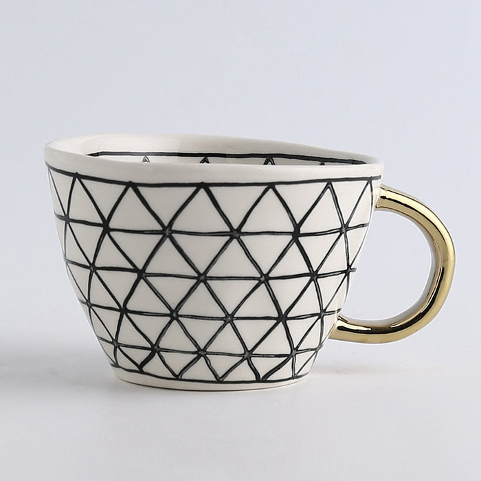 Ceramic mug with geometric black pattern and gold handle on a light gray background