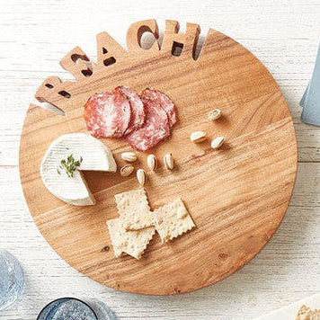 Round acacia wood beach cutting board with carved BEACH lettering styled with cheese and crackers