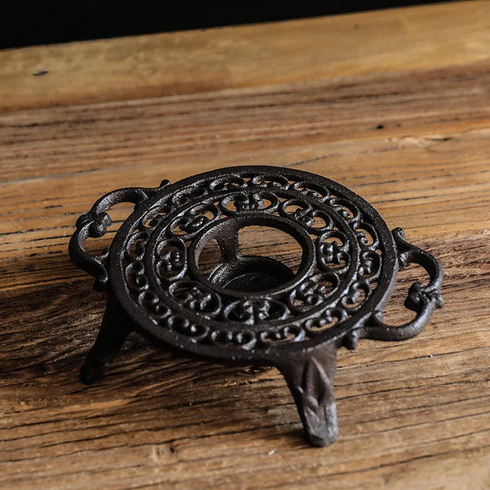 Cast iron circular tea light warmer stand with intricate scroll design and side handles on wooden surface