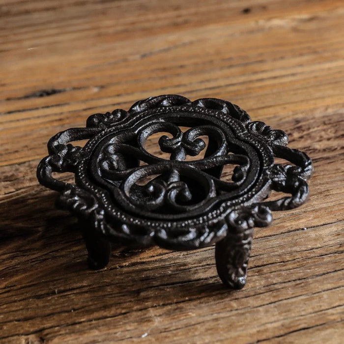 Cast iron flower-shaped tea light candle warmer stand with scroll detailing on wooden surface