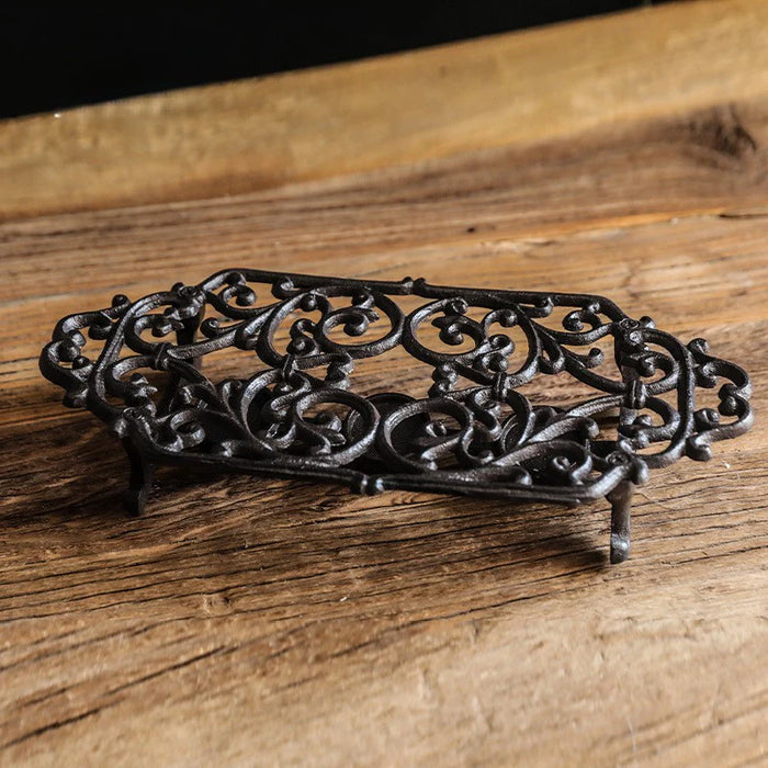 Cast iron rectangular tea light warmer stand with ornate scroll design on wooden surface