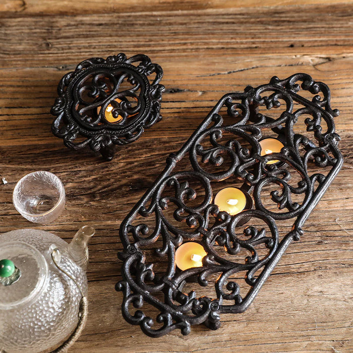 Cast iron tea light candle warmer stands with scroll detailing styled on wooden surface with teapot