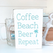 Handmade white wood sign reading Coffee Beach Beer Repeat with teal palm tree lettering displayed with a glass beer mug coastal decor