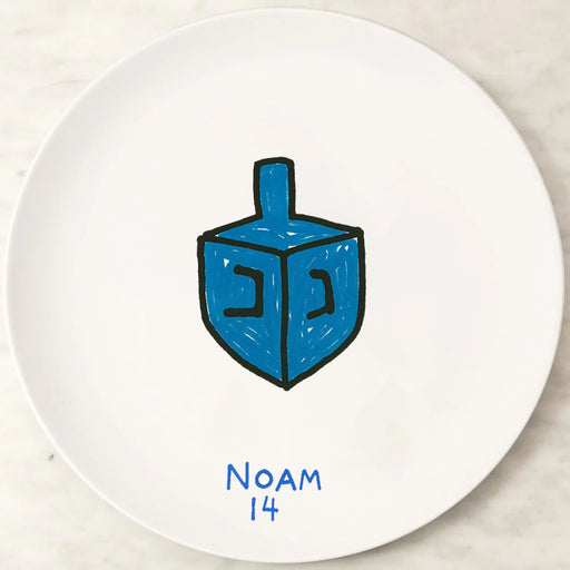 White plate with a blue dreidel and 'NOAM 14' text on a marble surface