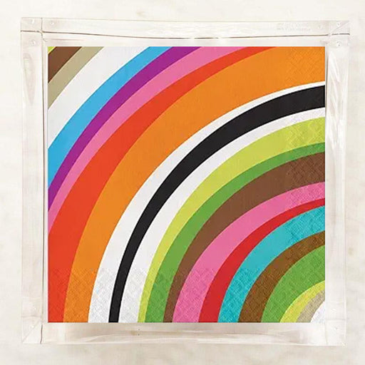 A square paper napkin featuring a vibrant multicolor rainbow stripe pattern, sealed in a clear plastic sleeve and displayed on a light marble surface.