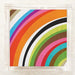 A square paper napkin featuring a vibrant multicolor rainbow stripe pattern, sealed in a clear plastic sleeve and displayed on a light marble surface.