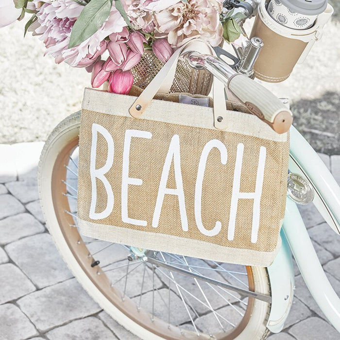 Mini jute beach tote bag with BEACH lettering, leather handles, and waterproof lining styled on a bicycle