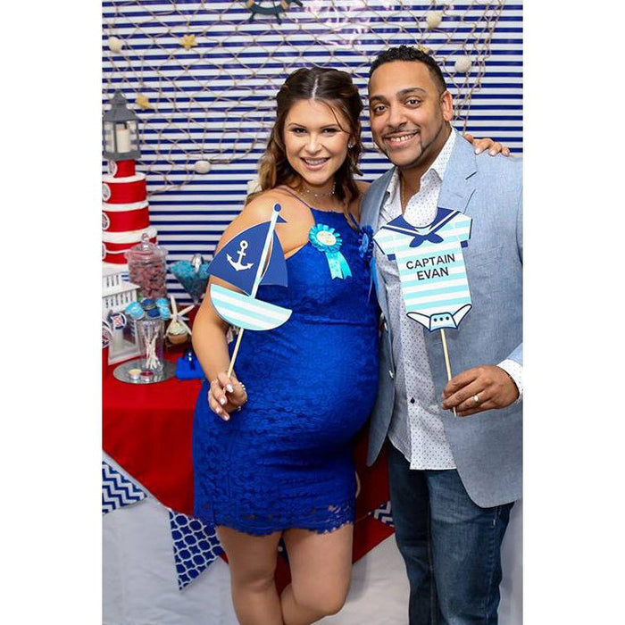 Expecting couple at nautical baby shower holding custom Captain onesie and sailboat photo booth props