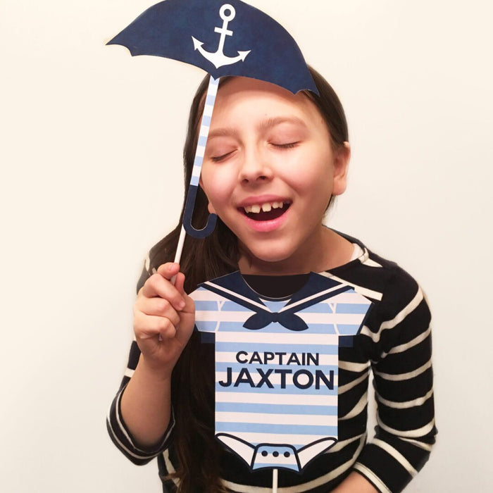 Girl holding navy nautical baby shower photo booth props including anchor umbrella and Captain onesie sign