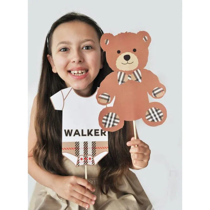 Girl holding preppy plaid baby shower printable photo booth props including teddy bear and onesie