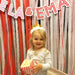 Retro red and white printable name banner spelling "ELA & EMA" hanging over a streamer backdrop with a young girl holding popcorn below