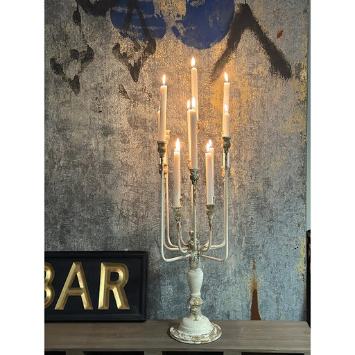 Vintage iron candelabra with 13 lit taper candles on a tabletop against a textured wall.