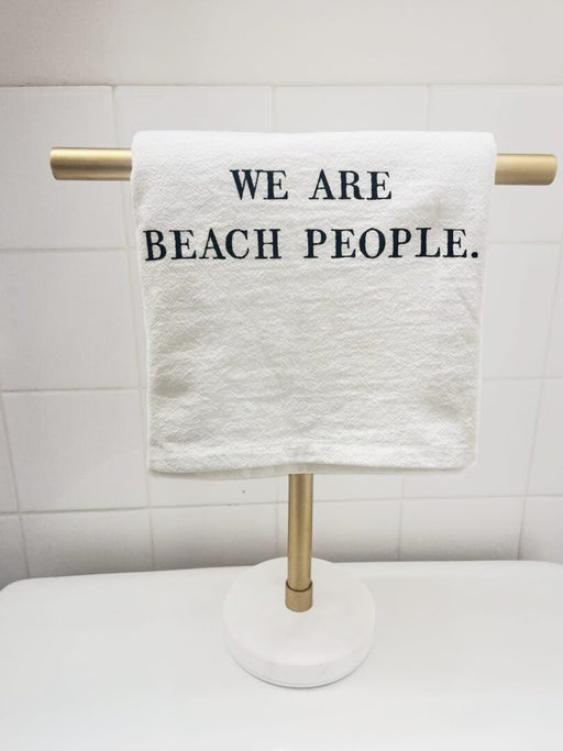 White cotton hand towel with We Are Beach People lettering on a gold towel stand